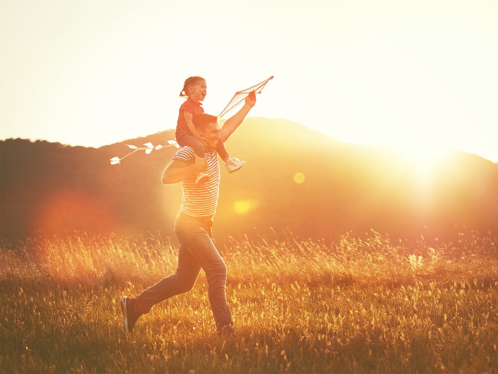 happy family father and child run on meadow with a kite in summer